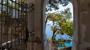 A stone staircase leading to a balcony with a metal gate, overlooking a body of water and trees. - Villa Flaminia by My Villa Collection (Capri)
