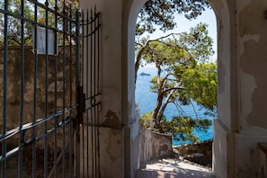 A stone staircase leading to a balcony with a metal gate, overlooking a body of water and trees. - Villa Flaminia by My Villa Collection (Capri)