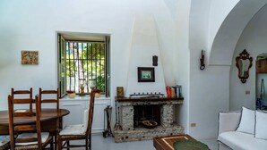 A dining area with a stone fireplace, a white sofa, and a window with bars. - Villa Flaminia by My Villa Collection (Capri)