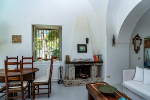 A dining area with a stone fireplace, a white sofa, and a window with bars. - Villa Flaminia by My Villa Collection (Capri)