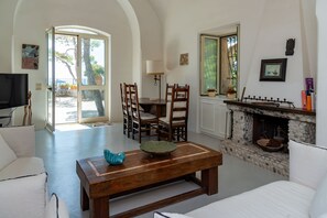 A living room with a fireplace, a dining area with chairs, a sofa, and a television. - Villa Flaminia by My Villa Collection (Capri)