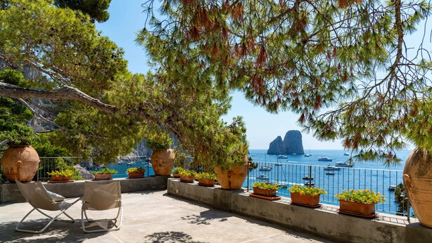 A terrace with chairs, potted plants, and a view of the sea. - Villa Flaminia by My Villa Collection (Capri)