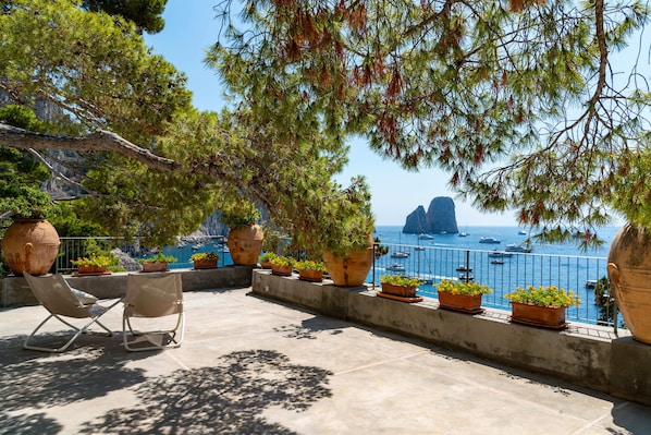 A terrace with chairs, potted plants, and a view of the sea. - Villa Flaminia by My Villa Collection (Capri)