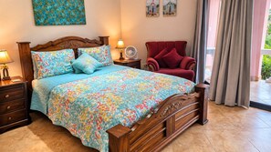 Een slaapkamer met een houten bed, bloemenbedekking, een rode fauteuil en uitzicht op het landschap.