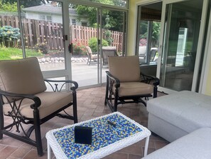 Eine Terrasse mit zwei Stühlen, einem Tisch mit Mosaikplatte und einer Glasschiebetür, die in einen Garten führt.