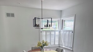 A dining area with a round table, six chairs, a vase with flowers, a modern chandelier, and a window with blinds. - Home on edge of Omaha Regency - 3-bedrooms 1.5 bath (Omaha)