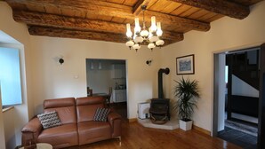 A living room with a brown leather sofa, a wooden ceiling, a chandelier, a fireplace, and a potted plant. - Unique Slovene alpine house, within the Soca Valley, close to Most na Soci. (Tolmin)