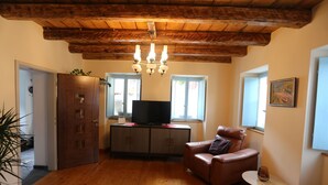 A living room with wooden flooring, a brown leather sofa, a television on a cabinet, and a chandelier. - Unique Slovene alpine house, within the Soca Valley, close to Most na Soci. (Tolmin)