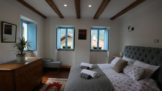 A bedroom with a bed, a dresser, a bench, and two windows with views. - Unique Slovene alpine house, within the Soca Valley, close to Most na Soci. (Tolmin)