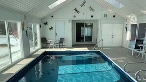 A swimming pool with clear water, surrounded by white walls and doors, with butterfly wall art and a patio area with chairs. - Deep Creek 365 Water Access 5 BR 5.5 BA Indoor Pool, Hot Tub, Theater, Dogs free (Swanton)