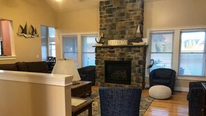 A living room with a stone fireplace, a sofa, a chair, and a lamp. - Deep Creek 365 Water Access 5 BR 5.5 BA Indoor Pool, Hot Tub, Theater, Dogs free (Swanton)