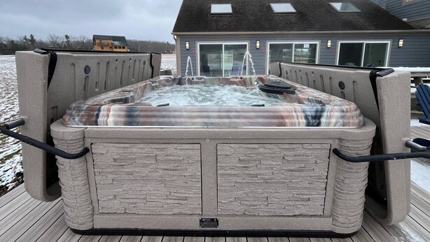 A hot tub with a stone-like exterior, a wooden deck, and a house in the background. - Deep Creek 365 Water Access 5 BR 5.5 BA Indoor Pool, Hot Tub, Theater, Dogs free (Swanton)
