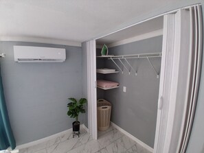 Ein Badezimmer mit Klimaanlage, einem Topf mit Pflanze, einer Wäscheleine und einem Mülleimer.