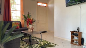 Uma sala de estar com sofá, mesa de centro, televisão e planta.
