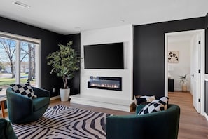 A modern living room with a fireplace, dark walls, and a large window.