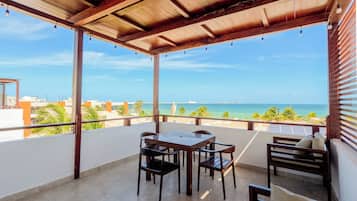 A covered outdoor area with a table and chairs, a view of the ocean, and a clear sky.