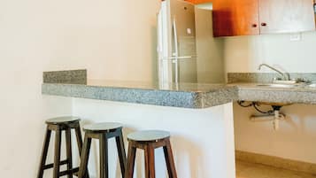 A kitchen with a granite countertop, a stainless steel refrigerator, wooden cabinets, and three bar stools.