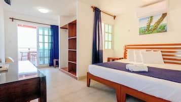 A hotel room with a bed, a desk, a chair, a wardrobe, and a painting on the wall.