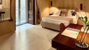 A hotel room with a bed, a desk, a chair, a chandelier, and a view through a door. - Aledo Boutique Apartments (Napoli)