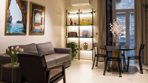 A modern living room with a sofa, dining table, chairs, and a bookshelf. - Aledo Boutique Apartments (Napoli)
