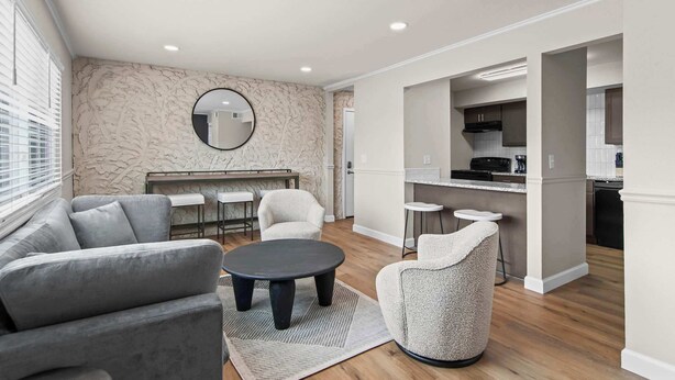A modern living room with a sofa, armchair, coffee table, and a dining area with a kitchen in the background. - Newly Renovated Unit in Central Spfld! #204 (Springfield)