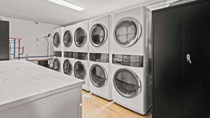 A laundry room with multiple washing machines, a marble countertop, and a black cabinet. - Newly Renovated Unit in Central Spfld! #204 (Springfield)