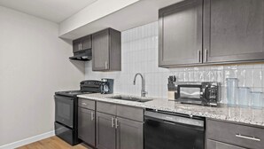 A modern kitchen with dark cabinets, a stainless steel dishwasher, a microwave, and a coffee maker. - Newly Renovated Unit in Central Spfld! #204 (Springfield)