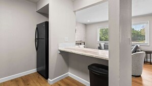 A kitchen with a black refrigerator, a countertop, a trash bin, and a window with blinds. - Newly Renovated Unit in Central Spfld! #203 (Springfield)