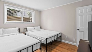 A bedroom with two beds, a window with blinds, a door, and a ceiling light.