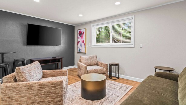 A modern living room with a flat-screen TV, two sofas, a coffee table, and a window with blinds.