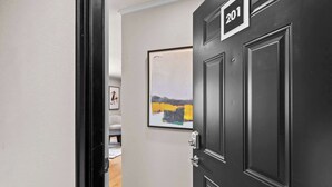 Un couloir avec une porte noire portant le numéro « 201 » et un tableau abstrait encadré accroché au mur.