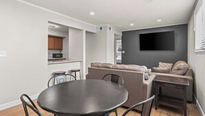 Uma sala de estar moderna com um sofá, uma mesa de jantar e uma cozinha ao fundo.