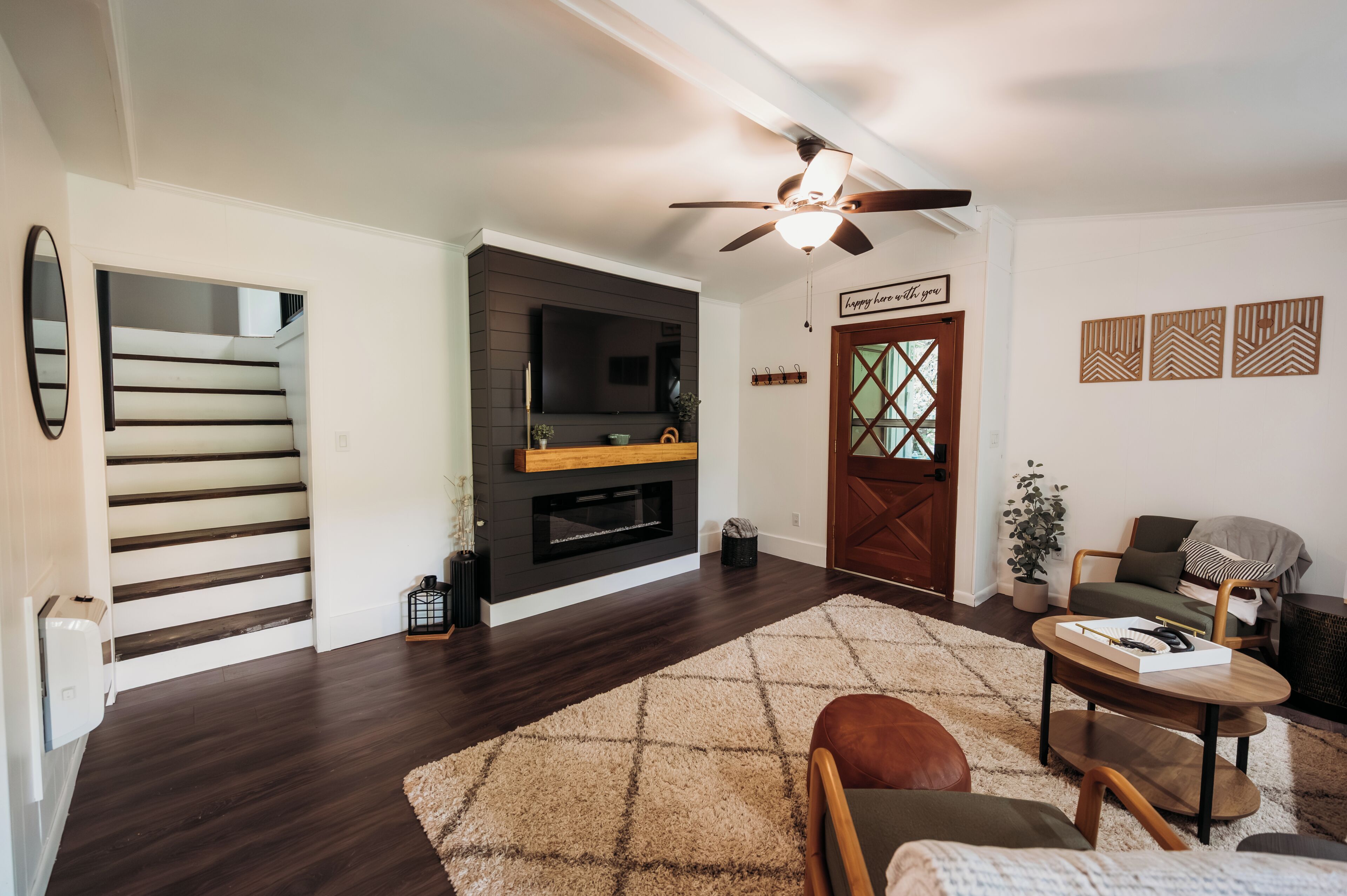 A living room with a fireplace, a ceiling fan, a staircase, and a door with a decorative glass panel.