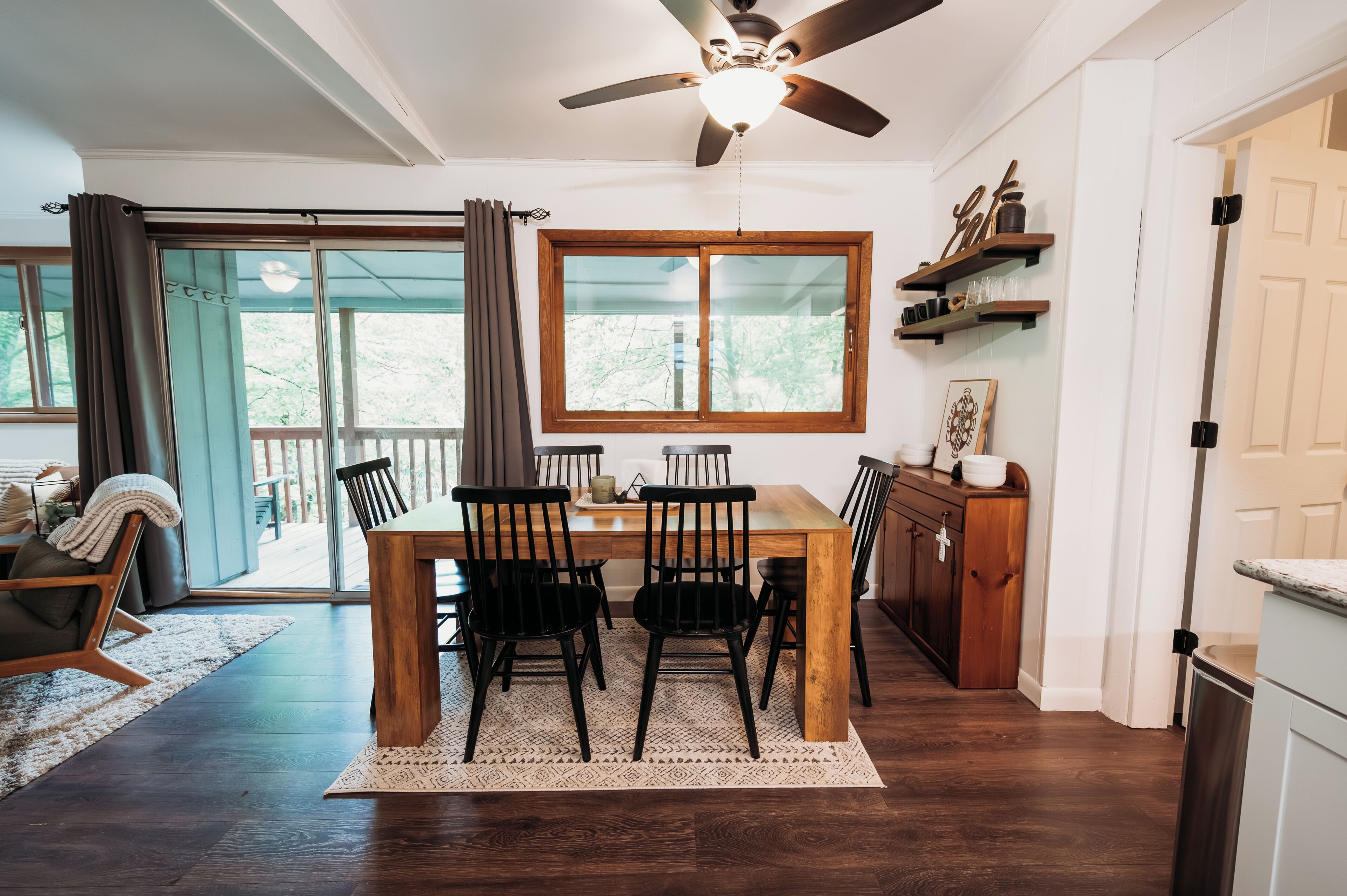 A dining area with a wooden table, black chairs, a ceiling fan, and a view through a glass door to the outside.