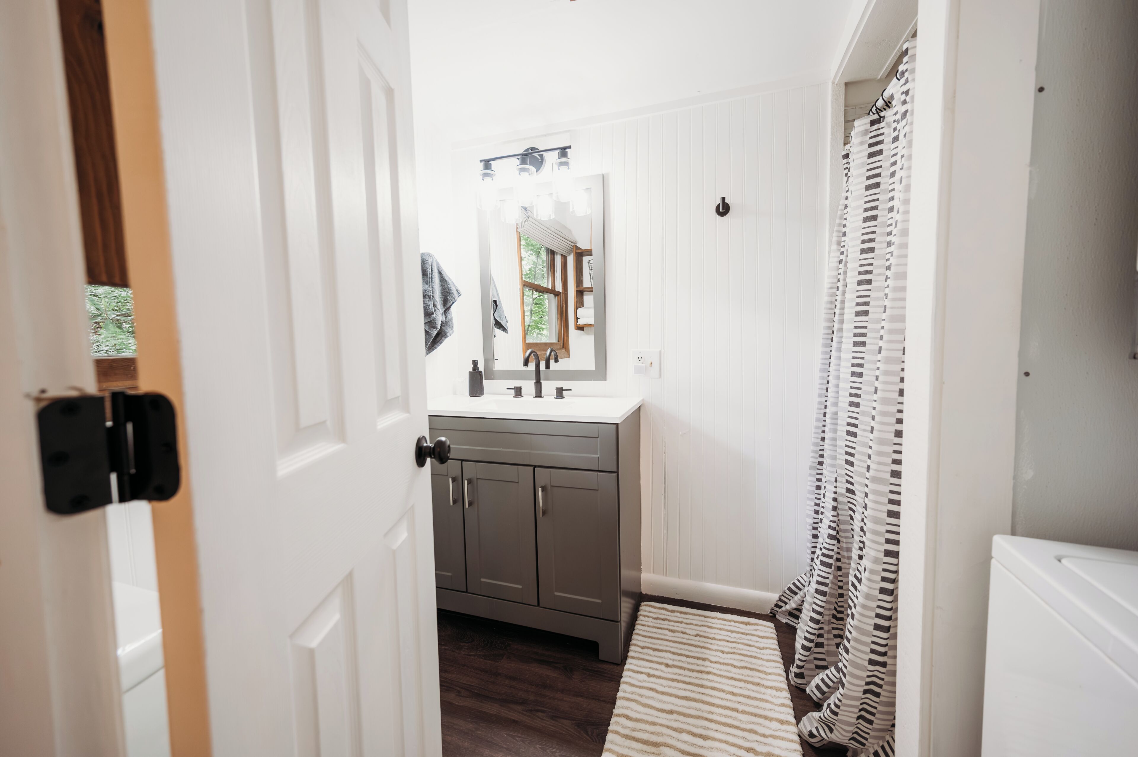 A narrow hallway leading to a bathroom with a sink, mirror, and a striped rug.