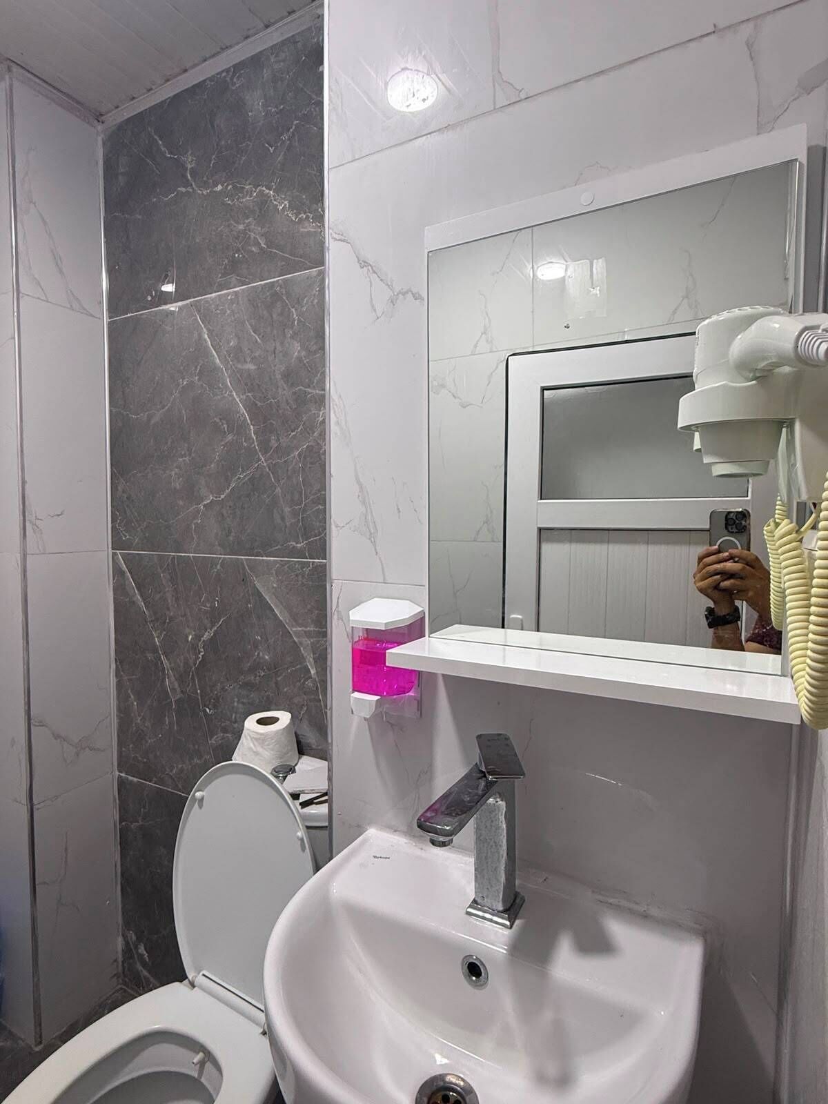A bathroom with a toilet, sink, mirror, and a hand dryer.