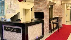 A reception desk with a 'Reception' sign, a brick wall, a flat-screen TV, and a red carpeted area. - Holiday Hotel (Erdemli)