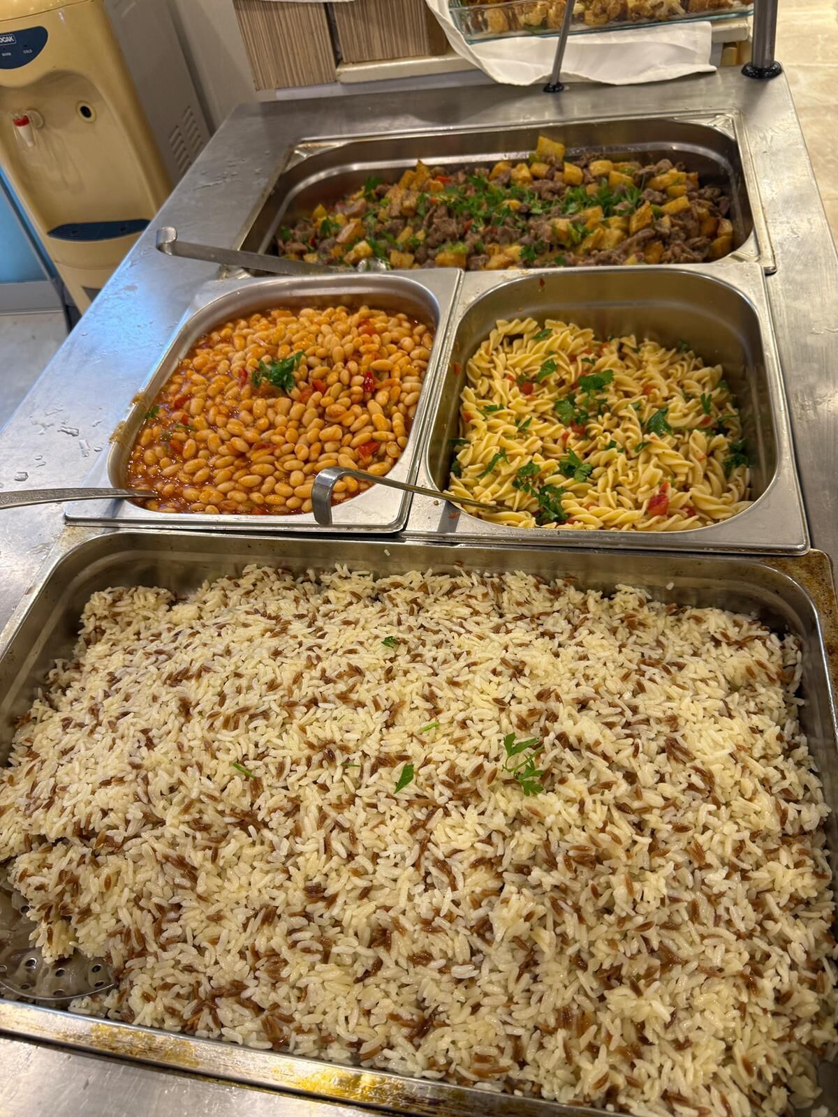 Un bufé con varios platos, incluyendo frijoles, pasta y arroz.