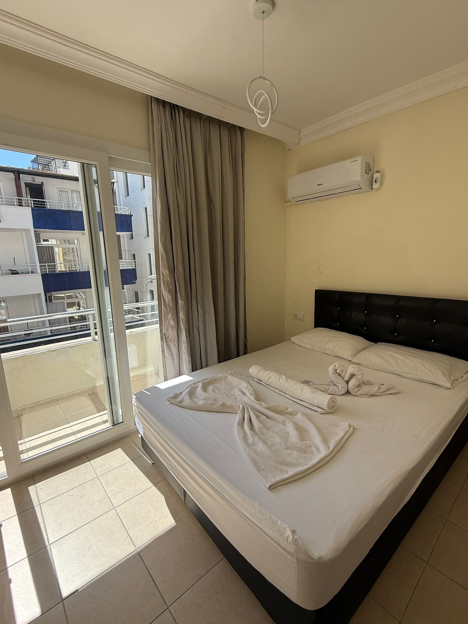 Habitación de hotel con cama, puerta corrediza al balcón y equipo de aire acondicionado en la pared.