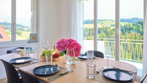 A dining area with a table set for two, a view of the countryside, and a balcony with a railing. - Nature & tranquillity I Bern I Family I Parking free I Pet-friendly (Köniz)