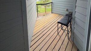 Une véranda couverte avec une terrasse en bois, une rambarde en métal et une seule chaise noire.