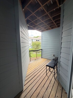 A covered porch with a wooden deck, a metal railing, and a single black chair. - Cozy 2-bedroom apartment and 4min walking distance to Mercedes-Benz Stadium (Atlanta)