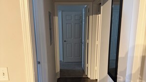 Un couloir avec un plancher en bois, des murs blancs et une porte au fond.