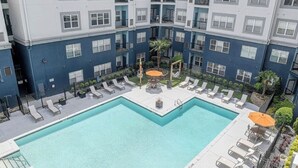 Un immeuble à plusieurs étages doté d’une piscine intérieure dans une cour centrale, d’un espace extérieur aménagé pour s’asseoir et d’un palmier.