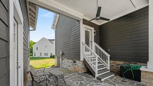 Une véranda couverte avec un sol en pierre, un banc, un escalier et un ventilateur.