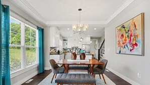 Un coin repas comprenant une table en bois, quatre chaises, un lustre et un grand tableau abstrait accroché au mur.