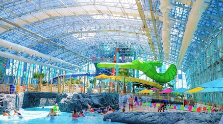 An indoor water park with a glass ceiling, slides, and a pool area.