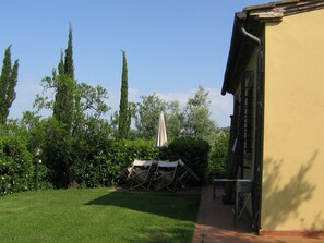 Ein Garten mit Rasen, einer Holzterrasse und einem Gebäude mit gelber Wand.