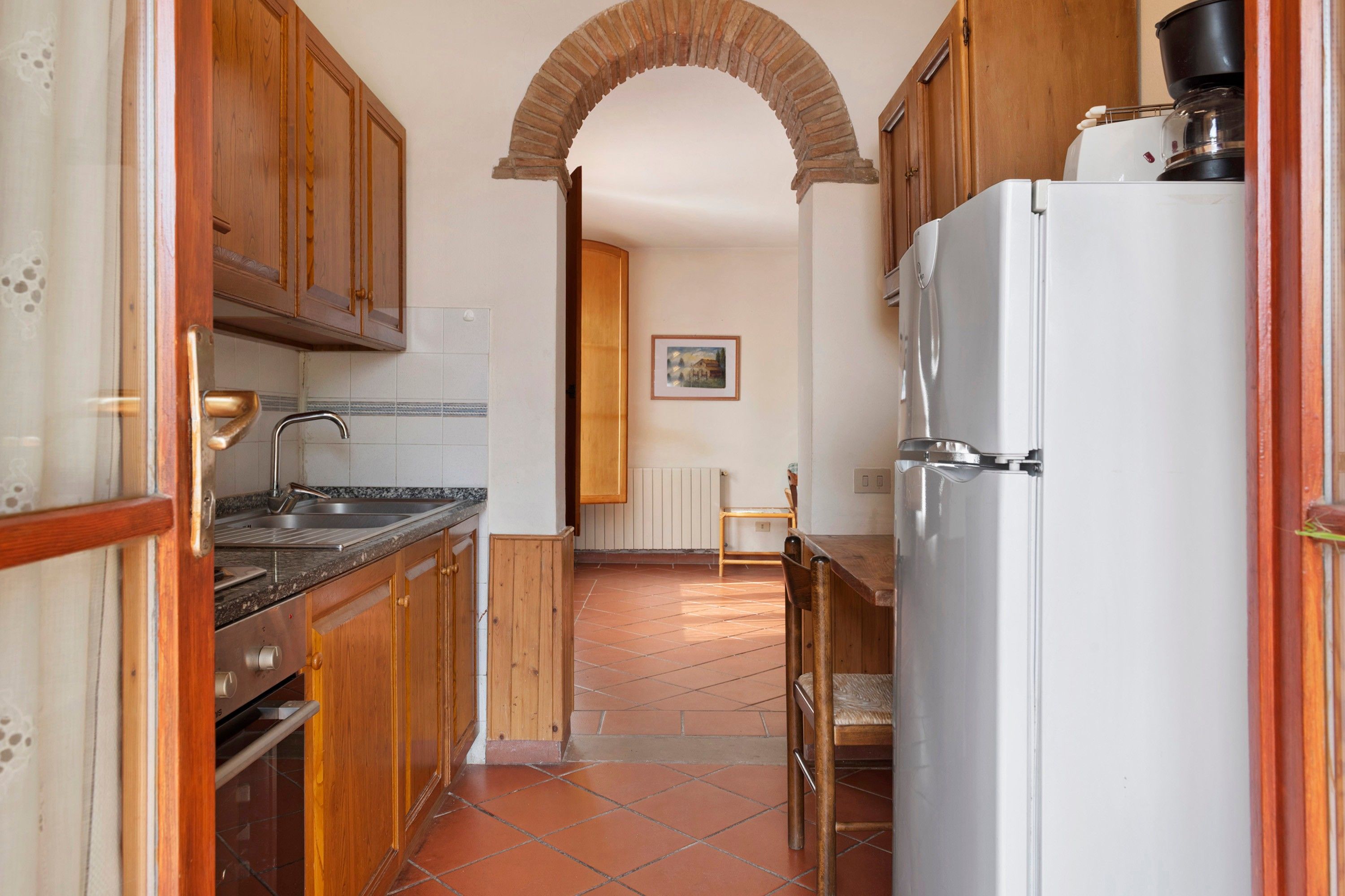 A kitchen with wooden cabinets, a white refrigerator, and a tiled floor.