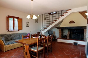 Ein Essbereich mit Holztisch und Stühlen, einer Couch, einem Kamin und einer Treppe.